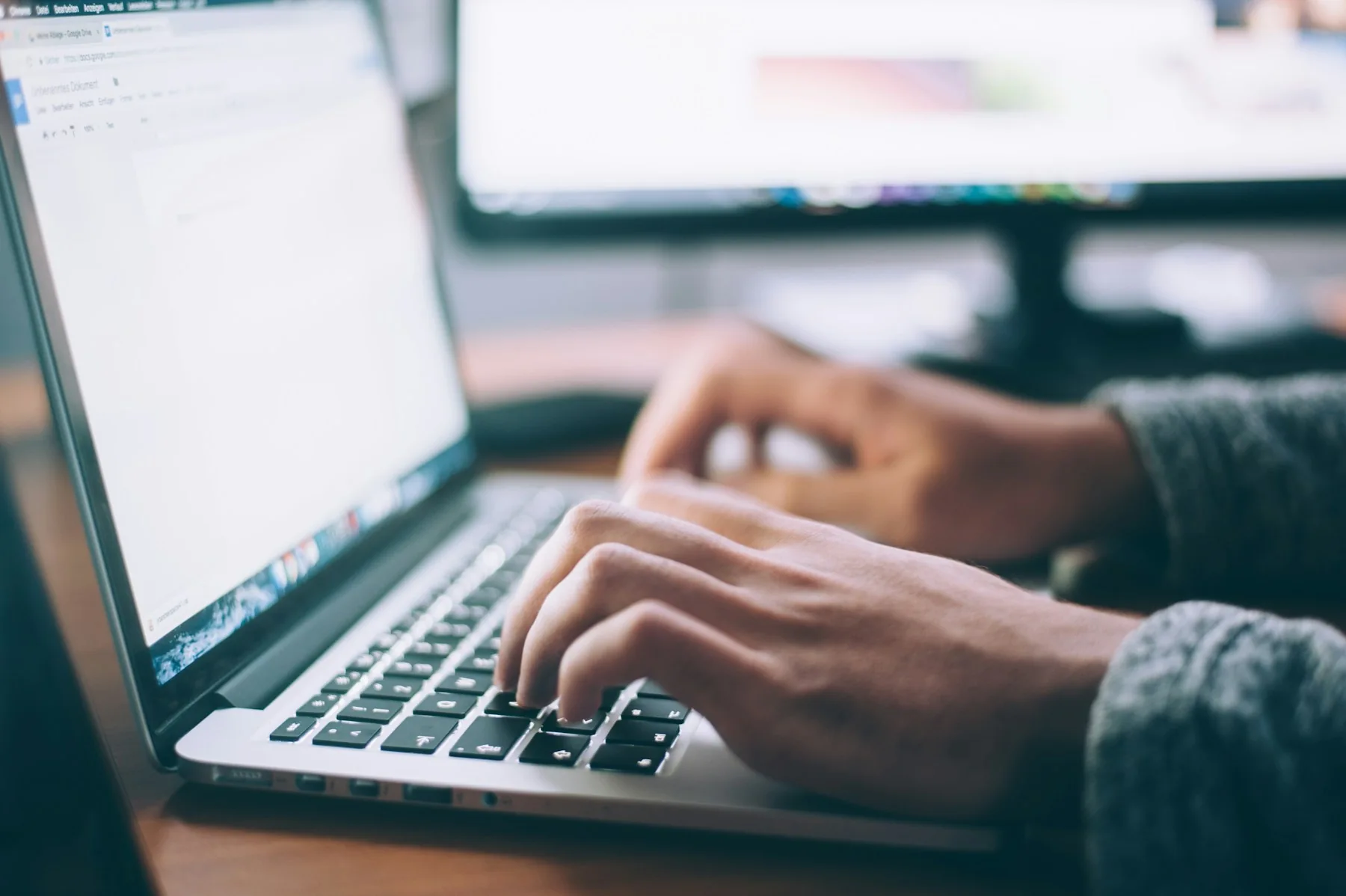 Hands typing on a laptop next to a notebook.